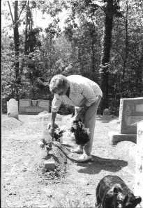 black and white photograph of older woman tending to mounded graves in cemetery
